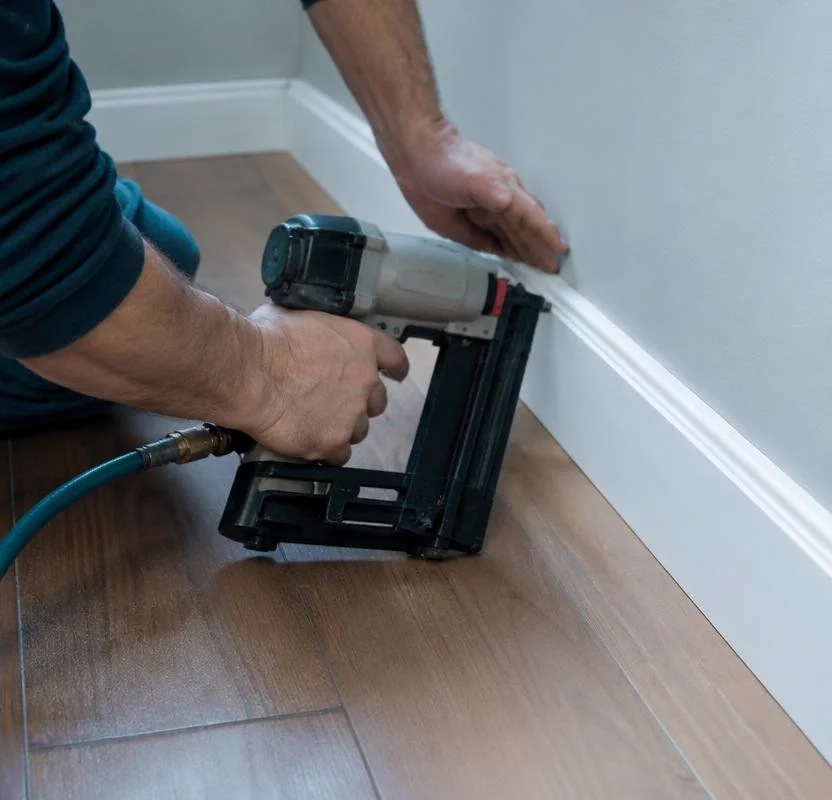 Carpenter installing white baseboard trim